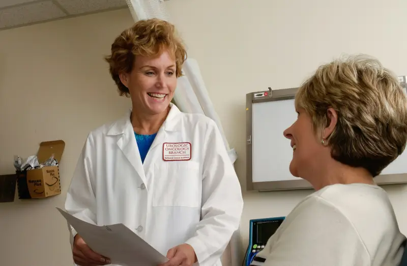 A smiling doctor in a white coat talks with an older patient in a clinic.