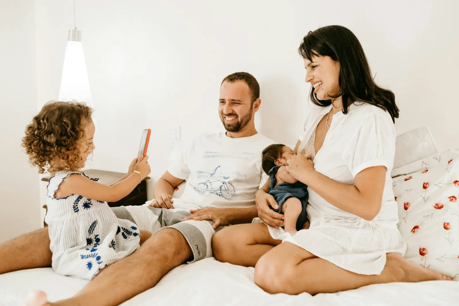 Parents with a toddler and a baby relaxing on a bed at home.