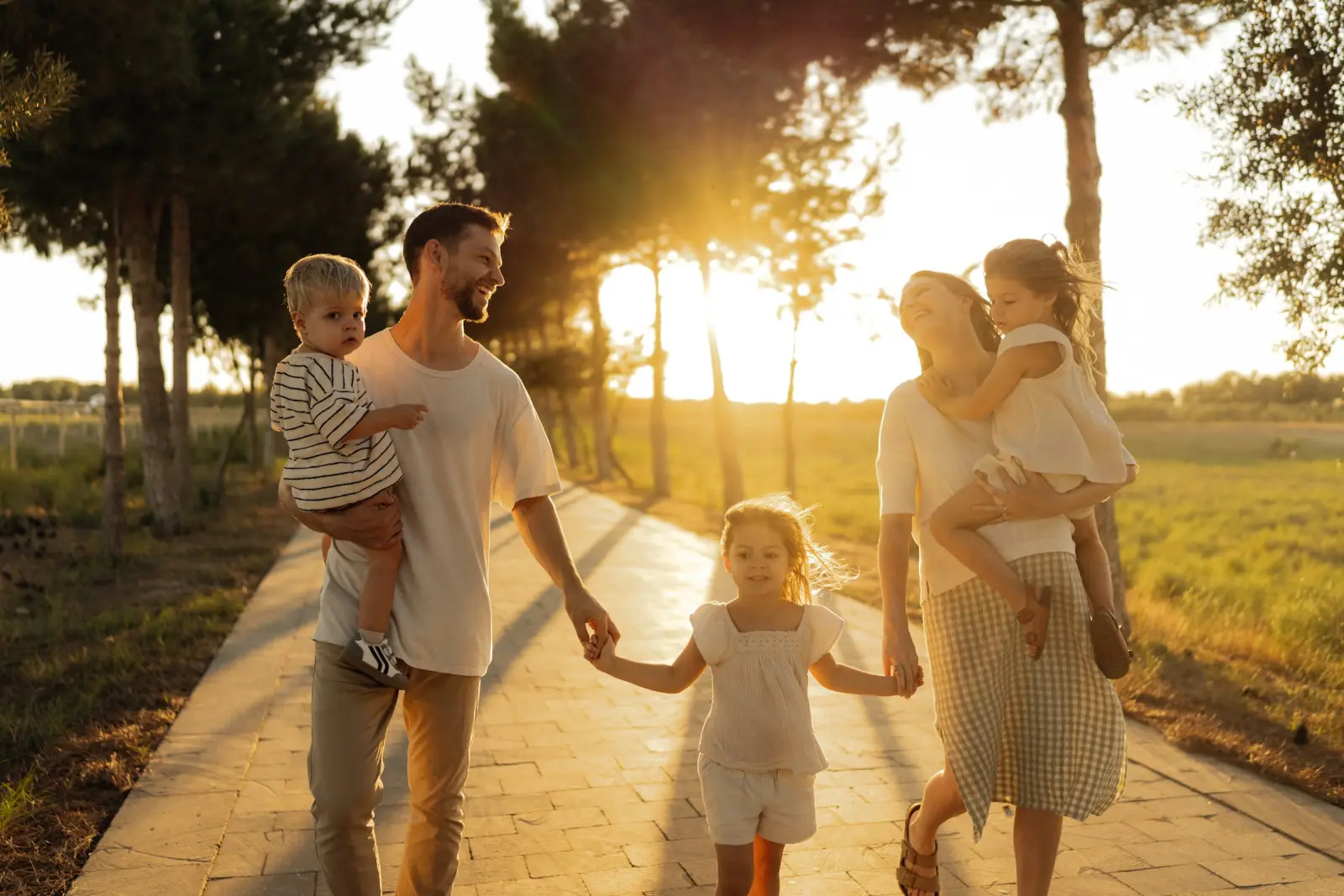 A family of five walks together down a tree-lined path at golden-hour sunset.