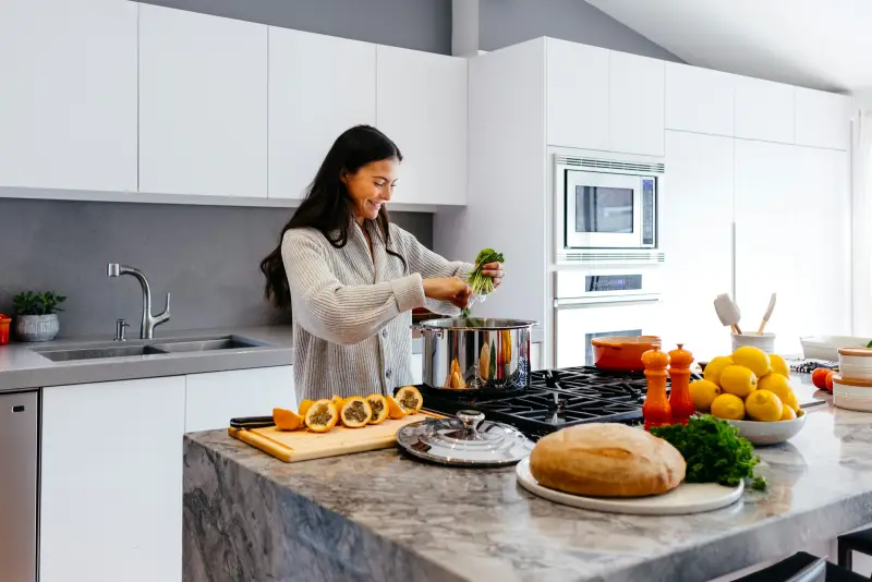 A woman smiles while cooking fresh food in a bright kitchen.